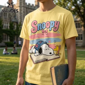 Yellow cotton t-shirt featuring Snoopy wearing a blue backpack and writing in a notebook next to Woodstock.!