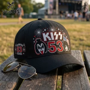 KISS Band 53 Years Anniversary black baseball cap with band member graphics, fireworks, and text on a wooden bench.