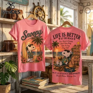Pink Snoopy graphic t-shirt featuring front beach surfing print and back lounge chair illustration on wood shelf background.!