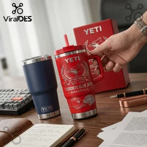 Red YETI tumbler with Toronto Blue Jays 50th anniversary logo and blue YETI tumbler on a desk with papers and a pen.!