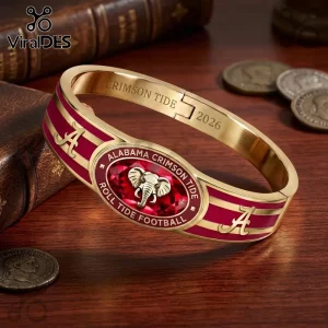 Alabama Crimson Tide 2026 Gold Plated Hinged Bracelet with crimson enamel, elephant logo, and engraved text on wood table.
