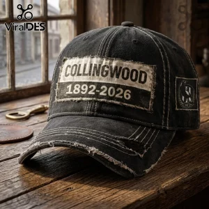 Collingwood Football Club 1892-2026 distressed black baseball cap featuring a vintage stitched patch on a wooden surface.
