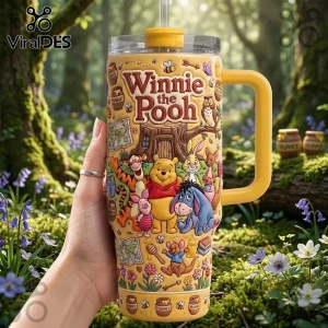 Winnie the Pooh Yellow 40oz Tumbler with character graphics, handle, and clear lid held in a hand in a forest setting.