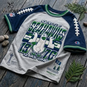 Seattle Seahawks 1976 Embossed Mascot Shirt in grey and navy with embroidered seagull graphics on a wooden surface.