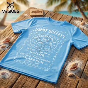 Jimmy Buffett Son of a Sailor blue t-shirt with white vintage rum label graphic, displayed on a wooden deck with sand.