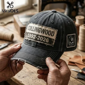 Collingwood Football Club 1892-2026 Distressed Black Baseball Cap with a vintage frayed patch on a workshop table.