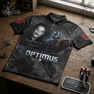 Peter Cullen Optimus Prime Black Tribute Polo Shirt featuring a portrait, robot graphic, and memorial text on wood surface.
