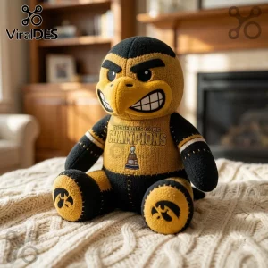Iowa Hawkeyes Mascot Heroes Game Champions plush toy in black and gold fabric with trophy graphic on a knitted blanket.