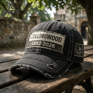 Collingwood Football Club 1892-2026 Distressed Black Baseball Cap with a frayed rectangular patch on a wooden bench.
