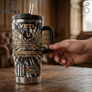 Collingwood Football Club 134th Anniversary YETI Tumbler with black and white tie-dye finish and team logo on wooden table.