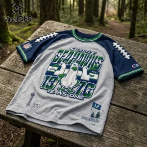 Seattle Seahawks 1976 Embossed Mascot Shirt in grey with blue sleeves, featuring seagull graphics on a wooden picnic table.