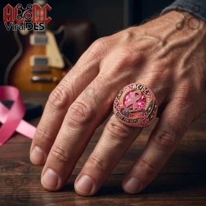 AC/DC Rock For Hope Breast Cancer Awareness Ring featuring a large pink gem, guitar emblem, and awareness ribbon on a hand.