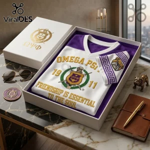 Omega Psi Phi 1911 Mascot V-Neck T-Shirt featuring gold lettering and Greek crest in a presentation box on a marble table.