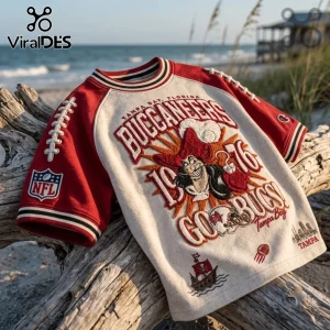 Tampa Bay Buccaneers 1976 Embossed Shirt featuring vintage pirate imagery, red sleeves, and NFL logo on a beach driftwood log.