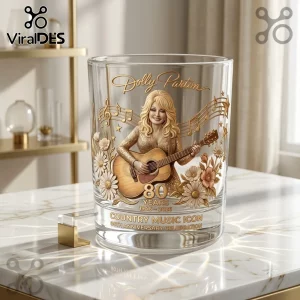 Dolly Parton 80th Anniversary Gold Whiskey Glass with a 3D relief of Dolly playing guitar, floral accents, and gold text.