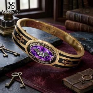 Ozzy Osbourne Prince of Darkness gold tone toggle bracelet with black inlay, purple oval gem, and iron cross detailing.