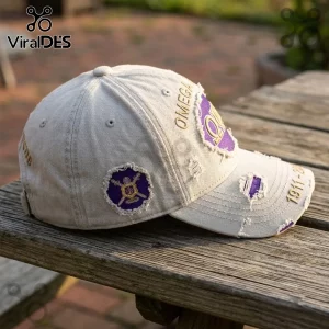 Omega Psi Phi 1911-2026 Distressed Baseball Cap in beige with purple embroidery and patches on a wooden surface.