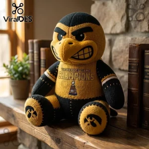 Iowa Hawkeyes Mascot Heroes Game Champions plush toy in black and yellow fabric sitting on a wooden shelf near books.