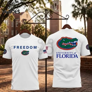 University of Florida Freedom White T-Shirt displaying an alligator logo, text, and US flag against a brick campus backdrop.