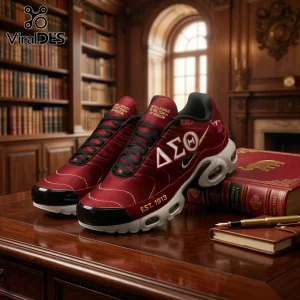 Delta Sigma Theta 1913 Crimson Air Max Plus shoes with gold Greek letters and EST. 1913 text on a wooden library desk.