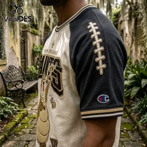 New Orleans Saints Mascot Embroidered Shirt featuring a football lace design on the sleeve and team branding on a cream tee.