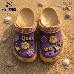 Omega Psi Phi Mascot Slip On Clogs With Charms in purple and gold with bulldog, 1911, and Greek letter accents on sand.