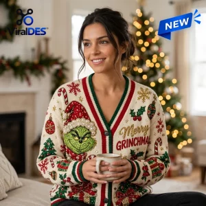 Woman wearing a cream colored Grinch Christmas 2026 ugly cardigan with red and green trim holding a coffee mug.