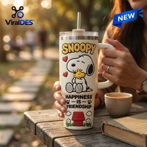 Person holding a Snoopy Happiness Is Friendship Stanley Tumbler 40oz on a wooden table outdoors.