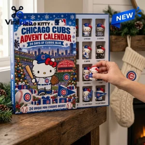 Hand picking a small figurine from an open Hello Kitty x Chicago Cubs 2026 Advent Calendar on a wooden table.