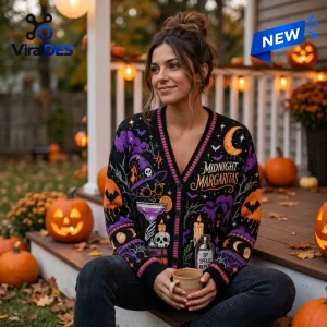 Front view of woman wearing a Midnight Margaritas Witch Cat Halloween ugly cardigan on a pumpkin-decorated porch.