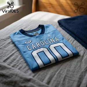 North Carolina Tar Heels Light Blue Custom Football Jersey with white numbers and ACC branding folded on a gray bedspread.