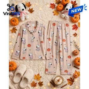 Flat lay of a beige pajama set with Snoopy pumpkin pattern surrounded by autumn leaves and miniature pumpkins.