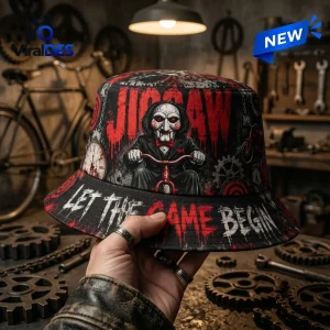 Hand holding a black horror bucket hat featuring red text and a creepy puppet illustration in a workshop setting.
