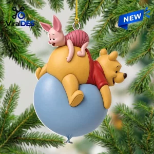Front view of a yellow bear and pink pig ornament hanging from a string against a blurred pine branch background.
