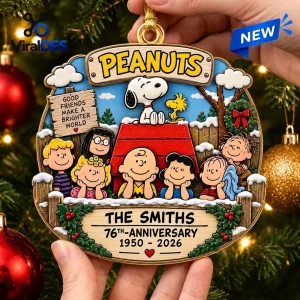 Peanuts 76th Anniversary Christmas ornament featuring Snoopy, the gang, and custom family name text on a festive wood sign.