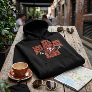 San Francisco 49ers Australia 2026 Kangaroo Mascot Hoodie in black featuring red and gold Melbourne 2026 game text on table.