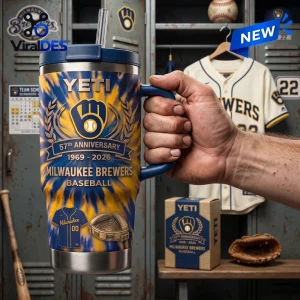 Close-up of a hand holding a blue and yellow tie-dye Milwaukee Brewers 57th Anniversary Stanley Tumbler in a locker room.
