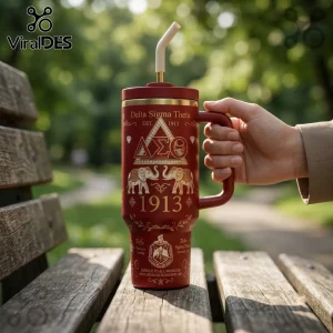 Delta Sigma Theta 40oz Crimson Gold Tumbler with handle, Greek letters, elephant motifs, and straw on a wooden bench.
