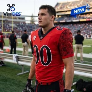 Man wearing a red San Diego State Aztecs football jersey with black patterned sleeves on a stadium field.