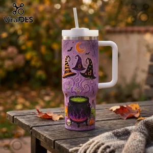 Halloween Magic Witches 40oz Handle Tumbler featuring purple finish, witch hats, a green cauldron, and bats on a wood table.