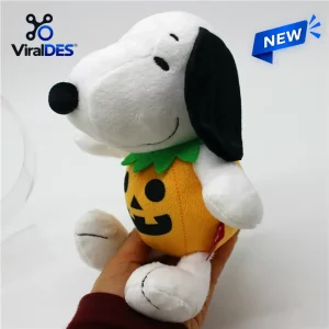 Side view of a white dog plush wearing an orange pumpkin costume with a green collar, held in a person's hand.