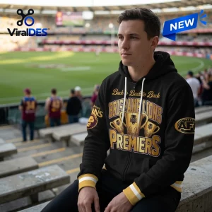 Man wearing a Brisbane Lions 2026 AFL Premiers black hoodie while seated in stadium stands.