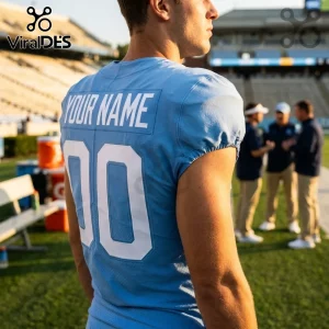 North Carolina Tar Heels light blue custom football jersey with white number 10 and nameplate on a stadium sideline.