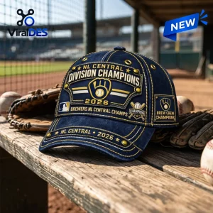 Front view of a blue Milwaukee Brewers 2026 Division Champions cap with yellow stitching on a wooden baseball dugout bench.