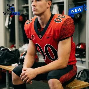 Athlete wearing a red San Diego State Aztecs personalized 2026 football jersey with black accents in a locker room.