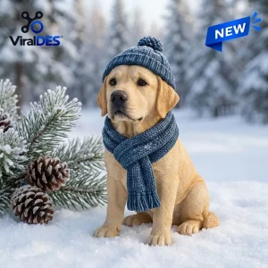 Front view of a yellow Labrador figurine wearing a blue winter beanie and scarf outdoors in snow.