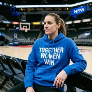 Front view of a woman wearing a blue Together Women Win hoodie while sitting on a basketball arena bench.