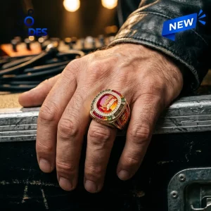 Closeup of a hand wearing the Def Leppard 2027 Tour Championship Ring against a dark stage background.