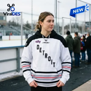 Front view of a woman wearing the PWHL Detroit 2026 Away Hoodie standing outdoors near an ice rink.