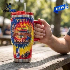 Hand holding a Red Bull 45th Anniversary YETI handle tumbler with colorful tie-dye pattern on a wooden picnic table.